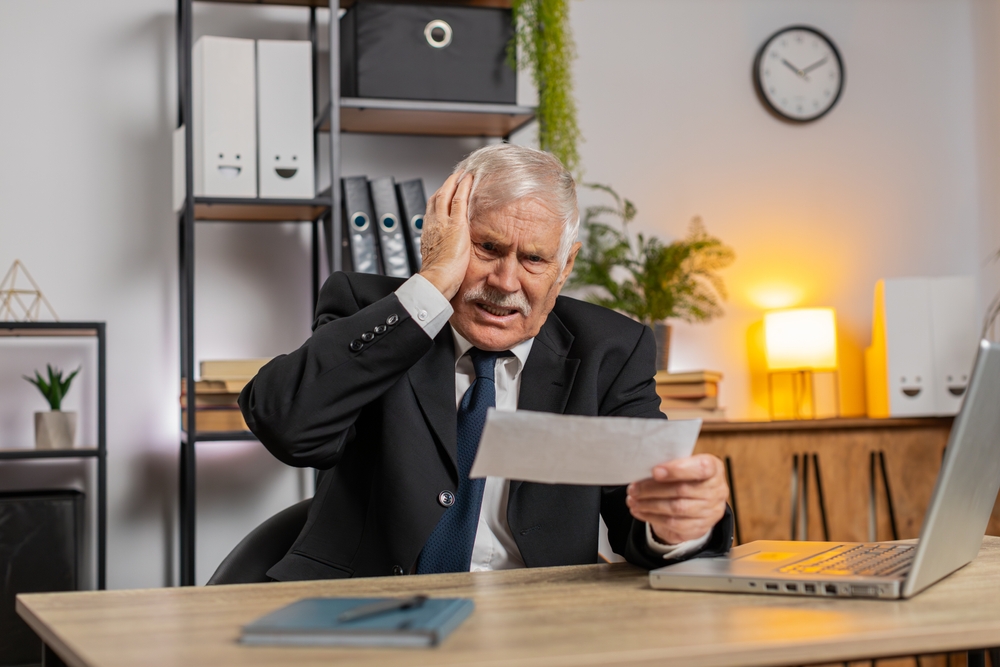 Choqué, le chef d'entreprise qui ouvre l'enveloppe en lisant les mauvaises nouvelles dans la lettre se sent contrarié. Problèmes financiers, dettes bancaires à payer, facture fiscale ou avis de faillite. Mec en costume à la table du bureau à domicile